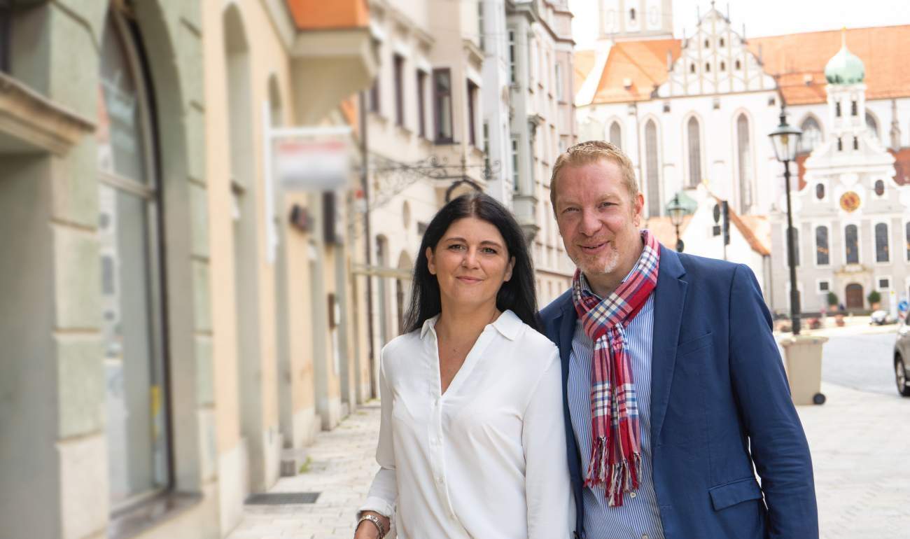 BONSENSA-GründerInnen und Geschäftsführende Sahra Holden und Oliver Foitzik vor der BONSENSERIA - BONSENSA Studio am Ulrichsplatz 10 in Augsburg, Basilika im Hintergrund