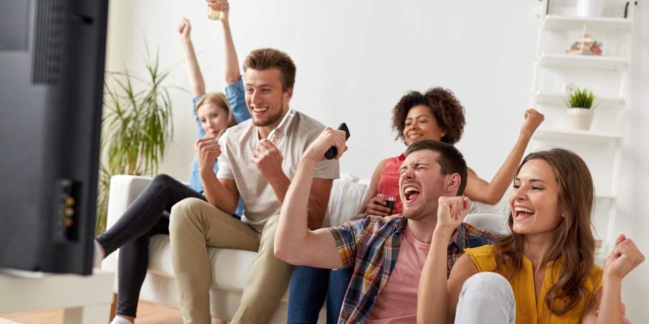 Gruppe von fünf Personen vor dem Fernseher freuen sich sehr und strecken die Fäuste in die Luft